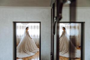 Jeune brunette dans longue mariage robe et voile dans Hôtel chambre. une charmant mariée, plein longueur, dans une magnifique blanc robe sur le Matin avant le mariage. photo