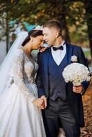 charmant et élégant jeunes mariés sont étreindre et souriant contre le Contexte de l'automne la nature dans une magnifique jardin. un incroyablement magnifique Jeune la mariée penché contre le épaule de sa bien-aimée jeune marié photo