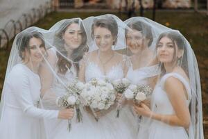 mariage la photographie dans la nature. une brunette la mariée et sa copines pose en dessous de une voile, en portant bouquets photo