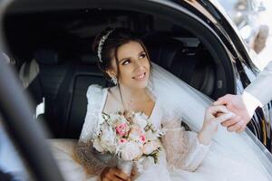 une magnifique mariée, séance dans une voiture, donne sa main à sa mari. une magnifique la mariée avec une bouquet de fleurs dans sa mains est séance dans une élégant coûteux auto. photo