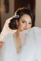 portrait de un incroyablement magnifique fille la mariée dans une blanc peignoir dans le chambre à coucher, le la mariée pose dans le Matin avant le mariage cérémonie. photo