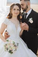 une Jeune la mariée et jeune marié tendrement embrasse dans le des rayons de le l'automne Soleil. soumissionner et magnifique Jeune fille la mariée. une homme baisers le sien bien-aimé. contre le Contexte de une magnifique jardin photo