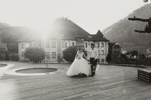 mariage noir et blanc portrait. le jeune marié dans une noir costume et le blond la mariée sont en marchant sur le Contexte de le Montagne et bâtiments, près le bassin. longue robe dans le air. photo