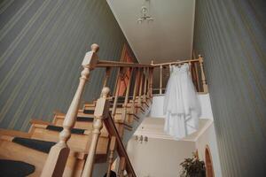 une délicat mariage robe bloque sur une magnifique balustrade dans le couloir de le maison. agréable lumière. mariage photo. une haute qualité photo