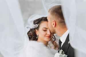 une Jeune la mariée et jeune marié tendrement embrasse dans le des rayons de le l'automne Soleil. soumissionner et magnifique Jeune fille la mariée. une homme baisers le sien bien-aimé. contre le Contexte de une magnifique jardin photo