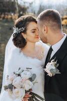 une Jeune la mariée et jeune marié tendrement embrasse dans le des rayons de le l'automne Soleil. soumissionner et magnifique Jeune fille la mariée. une homme baisers le sien bien-aimé. contre le Contexte de une magnifique jardin photo