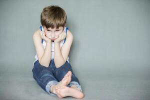 triste enfant d'âge préscolaire séance sur le sol. une ennuyé enfant. dérangé peu garçon. photo