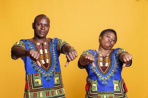 homme et femme montrant les pouces vers le bas geste tandis que donnant négatif la revue portrait. africain américain couple posant avec Ne pas aimer signe, mettant en valeur mal retour d'information et à la recherche à caméra photo