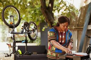 engagé amateur de sport noir femme à l'extérieur utilisant boîte à outils pour expert vélo réparation. Jeune en bonne santé africain américain femelle travail sur endommagé bicyclette avec professionnel équipements. photo