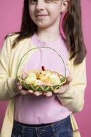 magnifique petit fille avec lapin oreilles en portant un Oeuf panier pour Pâques festivité, posant avec jolie printemps bibelots. content et énergique enfant célébrer le de fête saison dans le studio. photo