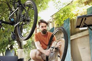 sportif et dévoué homme ajustement vélo engrenages avec professionnel équipement dans Accueil cour. actif caucasien Masculin réparations et maintient bicyclette Composants à l'extérieur en utilisant spécialisé outils. photo