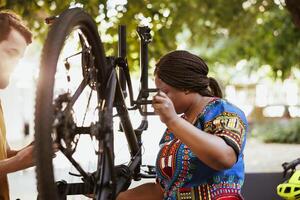 Jeune multiracial couple Faire entretien sur cassé bicyclette pneu avec travail outils dans Cour pour été vélo. Jeune couple Extérieur fixation vélo roue. photo