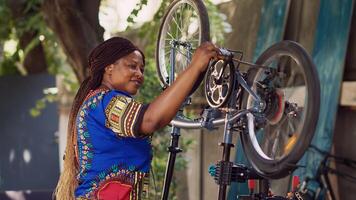 africain américain femme attentivement vérification bicyclette Composants assurer lisse et efficace été loisir vélo. souriant femelle cycliste performant vélo entretien. vue de côté portrait tir. photo