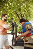 sportif Multi-éthnique couple inspecter et réparer bicyclette pneu et chaîne dans Accueil cour. en bonne santé et actif deux les personnes travail en plein air sur vélo entretien avec expert travail outil. photo