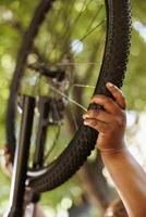 proche en haut de femelle africain américain main porter bicyclette roue pour annuel été entretien en plein air. en bonne santé la personne fixation et en changeant caoutchouc sur vélo pneu dans Accueil cour. photo