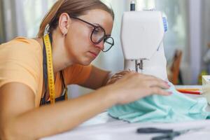 femme couturière dans des lunettes travaux sur machine à coudre à sa lieu de travail dans atelier photo