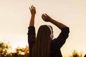 silhouette de Jeune femme dans écouteurs profiter la musique et dansant à le coucher du soleil photo