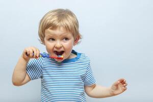 peu blond garçon brossage les dents avec brosse à dents sur bleu Contexte photo