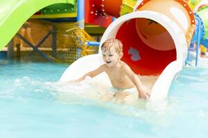 peu garçon en jouant sur l'eau faire glisser dans Extérieur bassin sur une chaud été journée photo