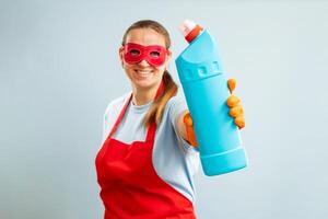 femme dans rouge masque, caoutchouc gants et tablier en portant nettoyage agent bouteille photo