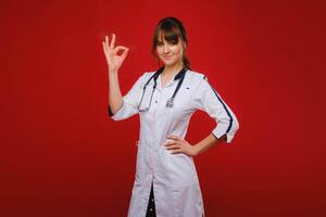 une Jeune médecin des stands sur une rouge Contexte et spectacles le sien main tout volonté être bien. le médecin spectacles d'accord. photo