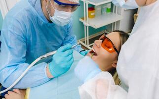 une Masculin dentiste avec dentaire outils exercices le les dents de une patient avec un assistant. le concept de médecine, dentisterie et soins de santé photo