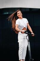 magnifique fille dans blanc élégant vêtements sur un électrique scooter dans le ville photo