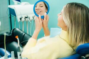 le fille sourit et regards dans le miroir dans dentisterie photo