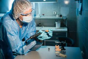 une masqué et ganté dentaire technicien travaux sur une prothétique dent dans le sien laboratoire photo