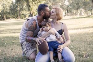 Jeune couple avec enfant ayant amusement à le parc avec le rugby Balle photo