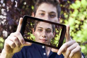 Jeune millénaire homme prise une selfie avec intelligent téléphone en plein air photo