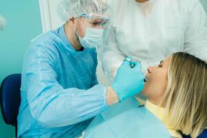 une Masculin dentiste avec dentaire outils exercices le les dents de une patient avec un assistant. le concept de médecine, dentisterie et soins de santé photo