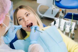 une dentiste dans une protecteur masque est assis suivant à lui et traite une patient dans le dentaire Bureau photo