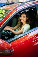 content souriant femme chauffeur derrière le roue rouge auto. vue par voiture fenêtre photo