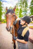 charmant Jeune femme portant casque caressant à sa marron cheval photo