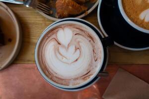 latté art et café tasses avec cannelle sur le tableau, accompagné par soucoupe, cuillère, et sucre une délicieux Matin boisson scène à le café photo