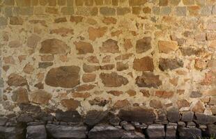 texture d'un mur de pierre avec de nombreuses grosses pierres brunes et grises armées de ciment. vieux fond de texture de mur de pierre de château pour un usage médiéval. partie d'un bâtiment en pierre photo