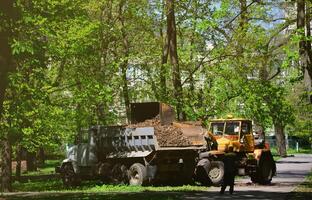 l'équipe d'amélioration de la ville enlève les feuilles mortes dans le parc avec une excavatrice et un camion. travaux saisonniers réguliers sur l'amélioration des lieux publics de loisirs photo