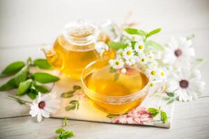 camomille fleur thé dans une verre tasse et théière, sur une en bois tableau. photo