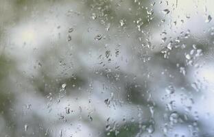 une photo de gouttes de pluie sur la vitre avec une vue floue des arbres verts en fleurs. image abstraite montrant des conditions météorologiques nuageuses et pluvieuses