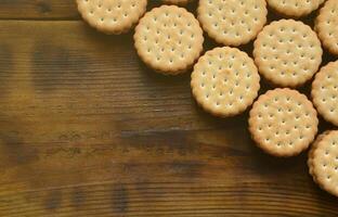 un biscuit sandwich rond fourré à la noix de coco se trouve en grande quantité sur une surface en bois marron. photo de friandises comestibles sur un fond en bois avec espace de copie