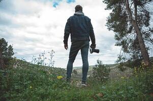 plein longueur portrait de une promeneur homme en portant caméra, admiratif le montagnes tandis que trekking dans le de bonne heure printemps la nature photo