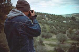 arrière vue Masculin Voyage photographe capturer magnifique de le montagnes om le sien professionnel numérique caméra tandis que randonnée photo