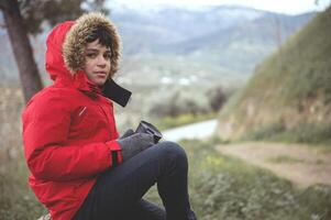 adolescent garçon en portant une thermos tasse, prise une Pause tandis que trekking dans montagnes photo