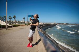 Jeune athlétique homme, sportif, repos, en buvant l'eau après une faire des exercices Extérieur. photo