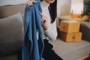 asiatique femme copains couple parler à caméra à vendre le vêtements à maison. Jeune attrayant affaires gens femelle vivre diffusion et montrant Vêtements à client dans en ligne vente au détail à Ventes à Bureau boutique photo