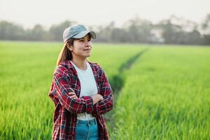 contenu femme agriculteur des stands avec plié bras dans le luxuriant vert riz des champs pendant le coucher du soleil. photo