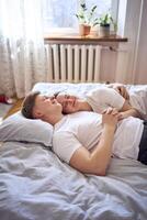 Jeune couple sur le lit en portant mains, une fille sur une garçons épaule, soumissionner câlins et touche photo
