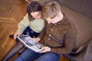 Jeune couple à la recherche à leur mariage photo album par le lit dans vivant chambre, cockapoo fonctionnement autour