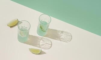 été scène fabriqué avec deux des lunettes de rafraîchissant boisson avec tranches de Frais citron vert contre brillant beige et pastel vert Contexte. minimal concept. branché heure d'été fête idée. été esthétique. photo